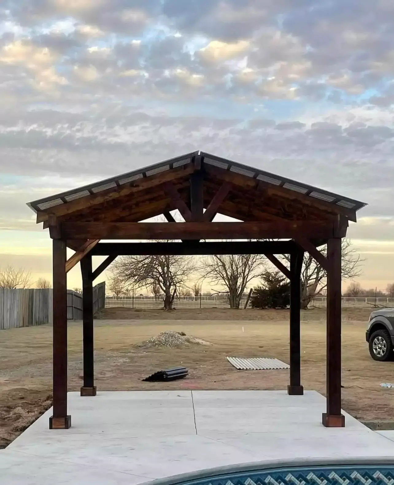 Wooden pergola on a concrete foundation in a large, open space.